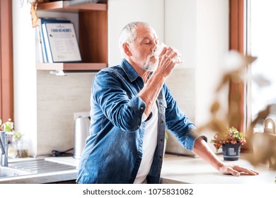Senior man drinking water in the kitchen.