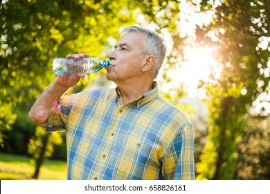 Senior Man Is Drinking Water In Park.