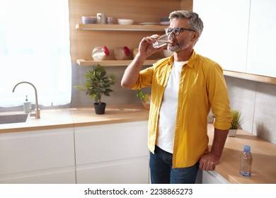 Senior Man Drinking Water. Portrait Of Mature Man With Glass Of Fresh Water At Kitchen. Health, Beauty and Water Balance Concept