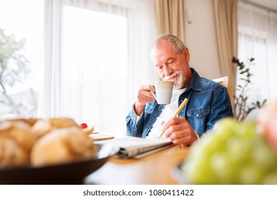 Senior Man Eating Breakfast And Doing Crosswords At Home.