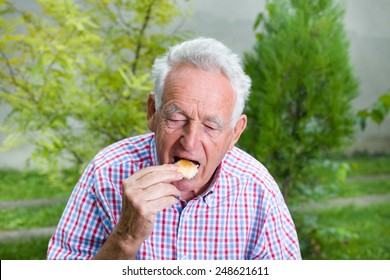 Senior Man Eating White Bread In Courtyard