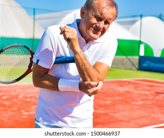 Senior Man With Elbow Pain Standing During Tennis Match On Sunny Day