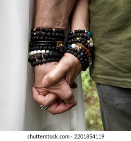 Senior Man En Woman Holding Hands. They Wear Lava Stone And Other Breaded Bracelets.