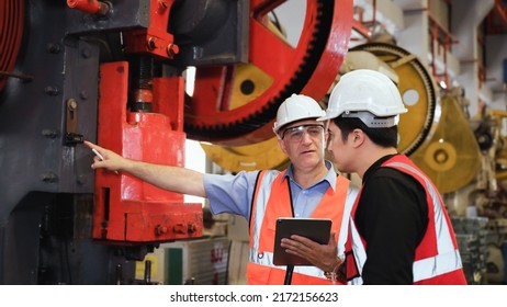 Senior man engineer wearing safety goggles and helmet standing holding tablet with coaching young engineer using hydraulic pump machine in factory. Two industry mechanic maintenance workers working. - Powered by Shutterstock