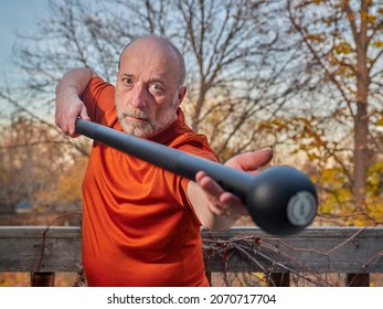 Senior Man Is Exercising With A Steel Mace In His Backyard, Selective Focus With Fall Scenery