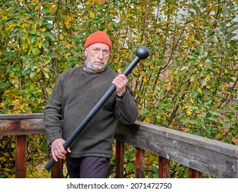 Senior Man Is Exercising With A Steel Mace In His Backyard, Chilly Autumn Afternoon