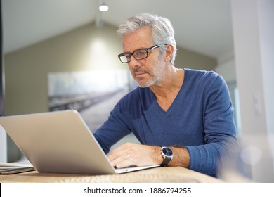 Senior Mann mit Brille verbunden mit Laptop zu Hause