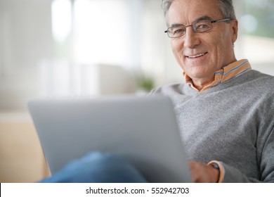 Senior man with eyeglasses connected on laptop at home