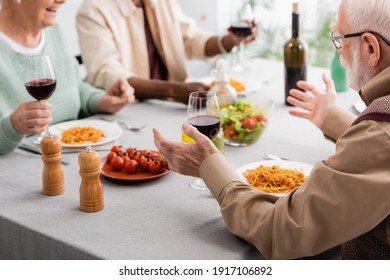 senior man in eyeglasses gesturing while having lunch with multicultural friends - Shutterstock ID 1917106892