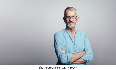 Senior man in eyeglasses isolated on grey background. Man standing with his arms crossed looking at camera. - Powered by Shutterstock