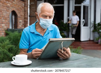 Senior man in face mask sitting at table in outdoor cafe with menu in hands. - Powered by Shutterstock