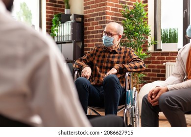 Senior Man With Face Mask Sitting In Wheelchair At Group Therapy Session. Person With Disability Attending Aa Meeting To Cure Alcohol Addiction And Receive Counseling During Pandemic.