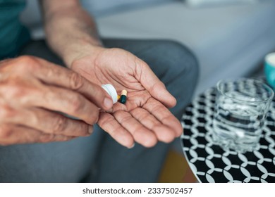 A senior man, feeling stressed and depressed, takes a pill with a glass of water. Depicting the act of self-medication and the impact of antidepressant drugs, use of medicines - Powered by Shutterstock