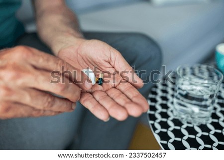 A senior man, feeling stressed and depressed, takes a pill with a glass of water. Depicting the act of self-medication and the impact of antidepressant drugs, use of medicines