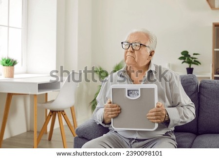 Senior man feels anxiety, doubts his unhealthy lifestyle, worries about health. Serious old elderly man on couch holding scales, thinking about body mass control, weight loss and calorie intake limit