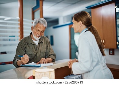 Senior man filling paperwork at reception desk while checking in for medical exam at doctor's office. - Powered by Shutterstock