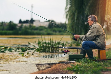 Senior man fishing on a freshwater lake sitting patiently on the shore with his rod and reel as he enjoys his retirement - Powered by Shutterstock