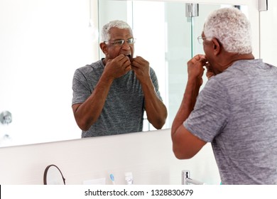 Senior Man Flossing Teeth Looking At Reflection In Bathroom Mirror Wearing Pajamas