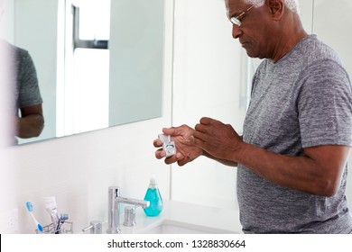 Senior Man Flossing Teeth Standing Next To Bathroom Mirror Wearing Pajamas