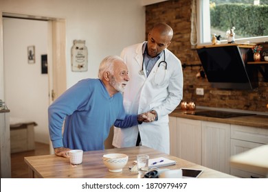 Senior Man Getting Up From The Chair With The Help Of African American Doctor At Nursing Home. 