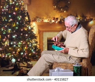 A Senior Man Gingerly Opening A Christmas Gift In A Decorated Living Room.