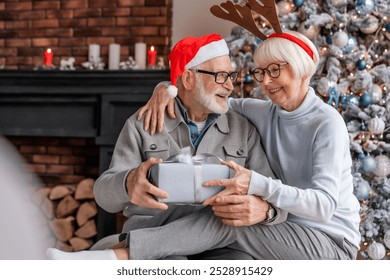 Senior man giving Christmas present to his wife. Elderly old couple grandparents spouses sharing giving gifts presents in the living room. Happy new Year celebration! - Powered by Shutterstock