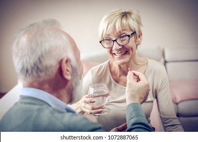 Senior Man Giving His Wife Medication Vitamins Supplement. 