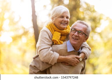 Senior Man Giving His Wife A Piggyback Outdoors
