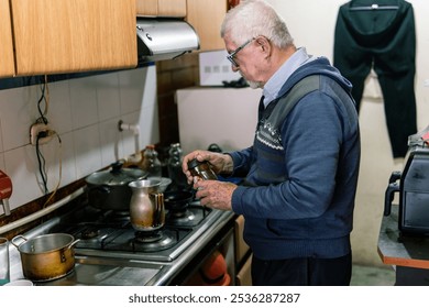 A senior man with glasses sprinkles spices into a coffee pot while cooking in a simple kitchen setting - Powered by Shutterstock