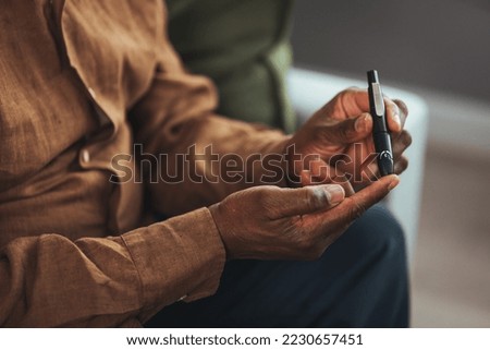 Senior man with glucometer checking blood sugar level at home. Elderly man testing for high blood sugar. Man holding device for measuring blood sugar. medicine, age, diabetes