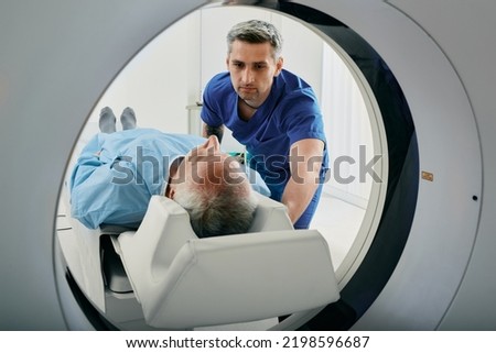 Senior man going into CT scanner. CT scan technologist overlooking patient in Computed Tomography scanner during preparation for procedure