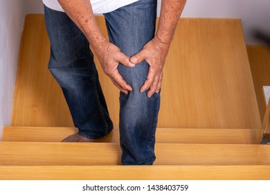 Senior Man Going Up The Stairs At Home And Touching His Knee By The Pain Of Arthritis. Health Care And Medical Concept.