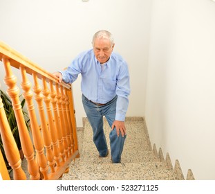 senior man going up the stairs at home and touching his knee by the pain of arthritis