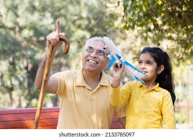 Senior Man With Granddaughter Having Fun Flying Toy Airplane At Park
