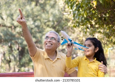 Senior Man With Granddaughter Having Fun Flying Toy Airplane At Park
