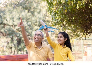 Senior Man With Granddaughter Having Fun Flying Toy Airplane At Park
