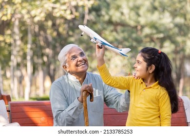 Senior Man With Granddaughter Having Fun Flying Toy Airplane At Park
