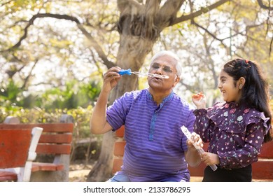Senior man with granddaughter having fun blowing bubbles at park
