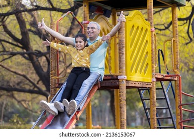 Senior man with granddaughter having fun while sliding in playground at park
