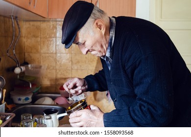 Senior Man Grandfather Old Pensioner Farmer Wearing Black Sweater And Hat Making A Cup Of Coffee Or Tea Cooking In The Pot At Home Putting Coffee To The Pot With Spoon