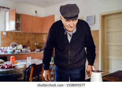 Senior Man Grandfather Old Pensioner Farmer Wearing Black Sweater And Hat Having A Cup Of Coffee Or Tea Cooking In The Pot At Home Waiting To Boil