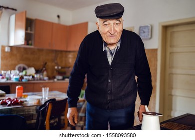 Senior Man Grandfather Old Pensioner Farmer Wearing Black Sweater And Hat Having A Cup Of Coffee Or Tea Cooking In The Pot At Home Waiting To Boil