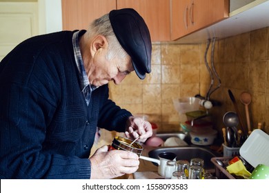 Senior Man Grandfather Old Pensioner Farmer Wearing Black Sweater And Hat Making A Cup Of Coffee Or Tea Cooking In The Pot At Home Putting Coffee To The Pot With Spoon