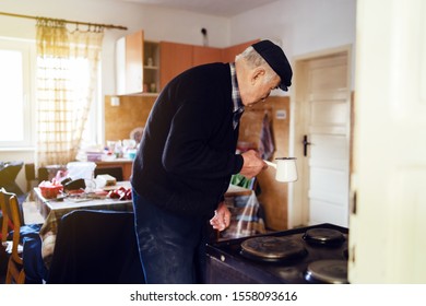 Senior Man Grandfather Old Pensioner Farmer Wearing Black Sweater And Hat Having A Cup Of Coffee Or Tea Cooking Carry The Pot At Home