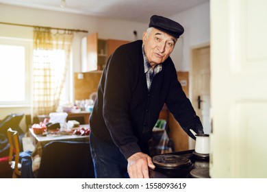 Senior Man Grandfather Old Pensioner Farmer Wearing Black Sweater And Hat Having A Cup Of Coffee Or Tea Cooking Carry The Pot At Home