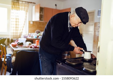 Senior Man Grandfather Old Pensioner Farmer Wearing Black Sweater And Hat Having A Cup Of Coffee Or Tea Cooking Carry The Pot At Home