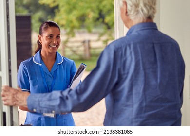 Senior Man Greeting Female Nurse Or Care Worker Making Home Visit In Uniform At Door