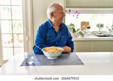 Senior Man With Grey Hair Eating Pasta Spaghetti At Home Looking Away To Side With Smile On Face, Natural Expression. Laughing Confident. 