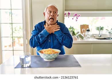 Senior man with grey hair eating pasta spaghetti at home shouting and suffocate because painful strangle. health problem. asphyxiate and suicide concept. 