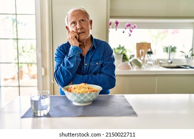 Senior Man With Grey Hair Eating Pasta Spaghetti At Home With Hand On Chin Thinking About Question, Pensive Expression. Smiling With Thoughtful Face. Doubt Concept. 